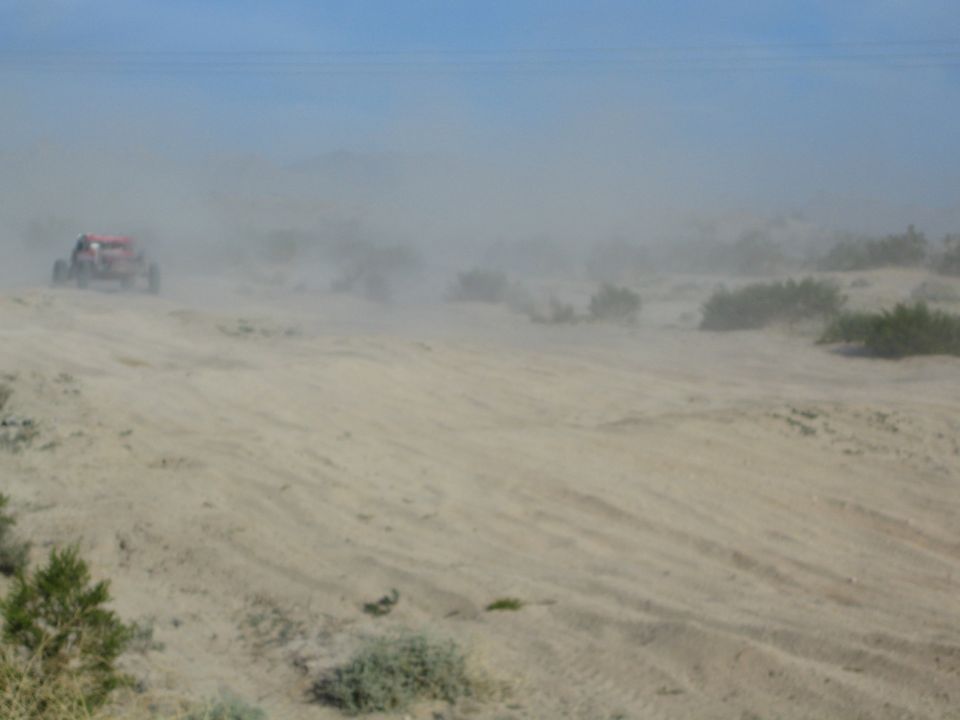 Distant red off-road buggy on a sandy desert ridge nearly hidden by dust haze