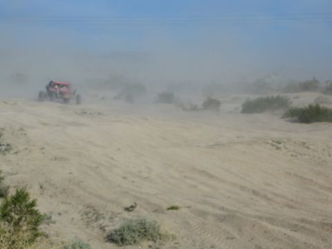 Red off-road buggy on a desert dune amid heavy dust haze
