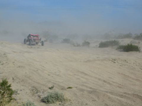 Red off-road buggy driving over a sandy desert rise in dusty conditions