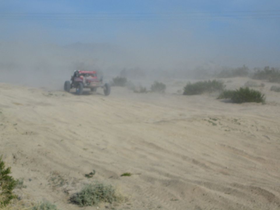 Red off-road buggy at distance crossing desert sand in a dust cloud