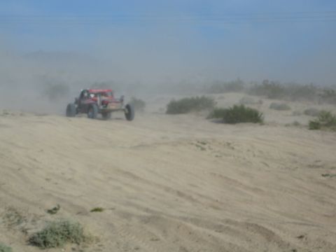 Red off-road buggy cresting a sandy desert dune with dust behind