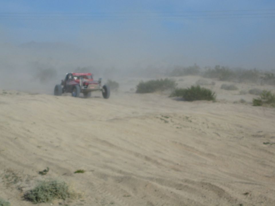 Red off-road buggy cresting a sandy desert dune with dust behind