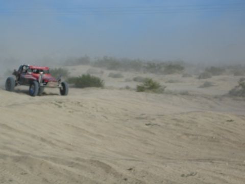 Red off-road buggy driving along a sandy desert ridge in dusty light