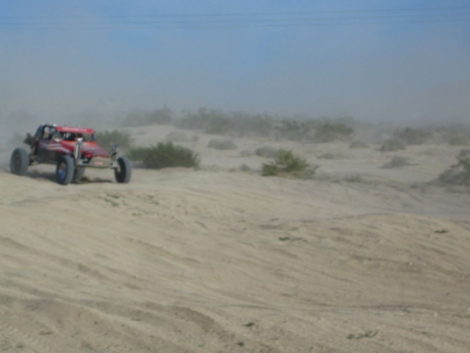 Red off-road buggy driving along a sandy desert ridge in dusty light