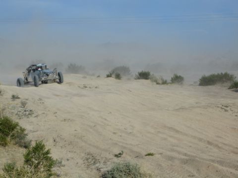 Silver-blue off-road buggy on a desert sand rise with dust haze behind