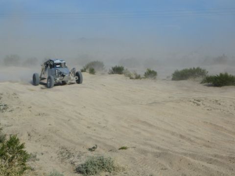 Gray tube-frame off-road buggy crossing desert sand with dust trailing