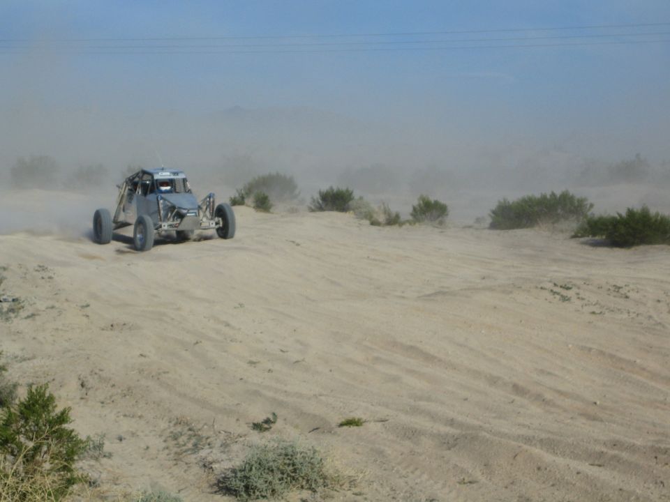 Gray tube-frame off-road buggy crossing desert sand with dust trailing