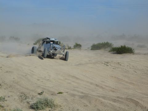 Gray off-road buggy at speed throwing sand on a desert wash