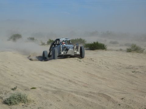 Gray off-road race buggy sliding through desert sand with antenna and dust