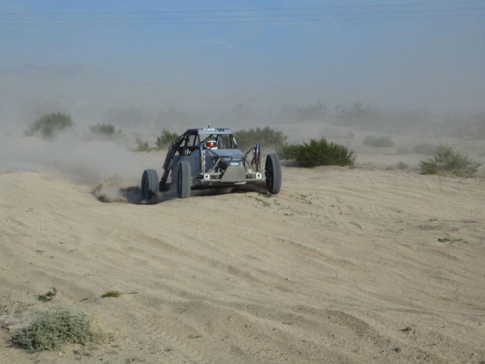 Gray off-road race buggy sliding through desert sand with antenna and dust
