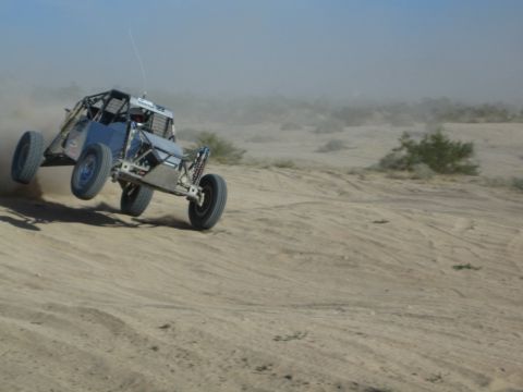 Gray off-road race buggy with front wheels lifting on desert sand at speed