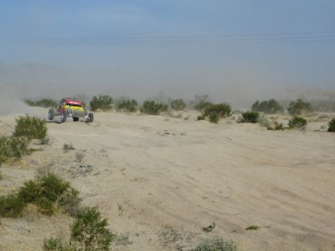 Distant red and yellow off-road buggy crossing desert brush and sand