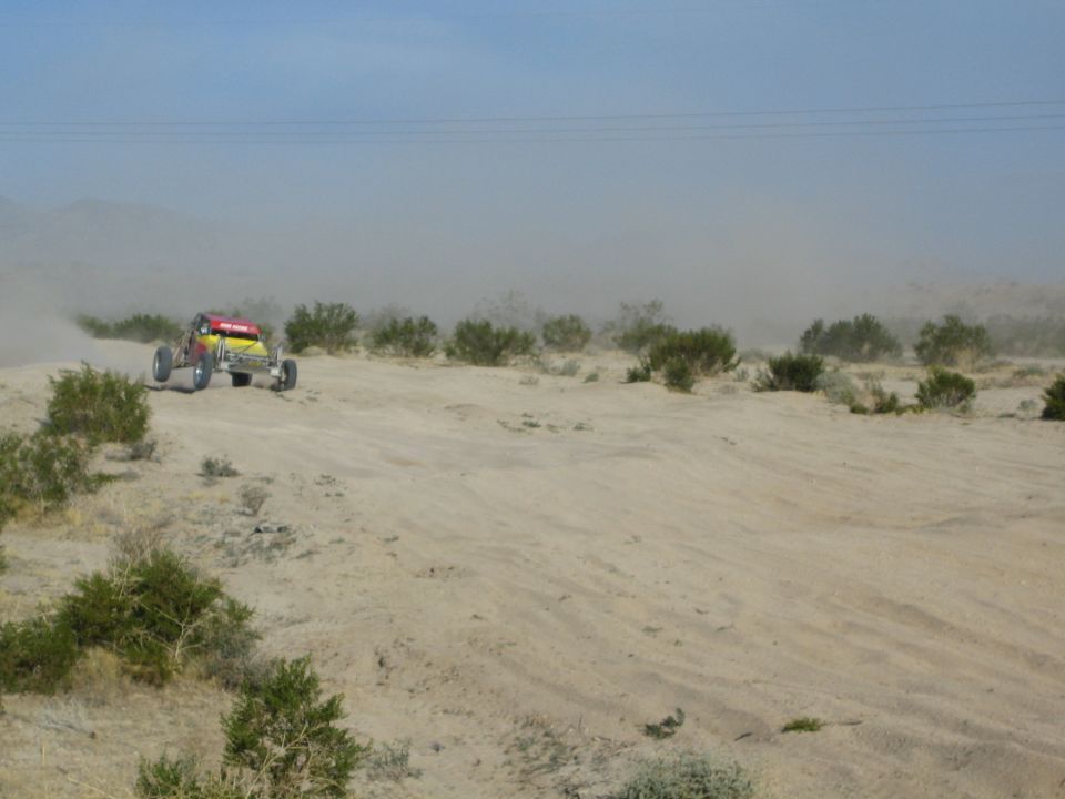 Distant red and yellow off-road buggy crossing desert brush and sand