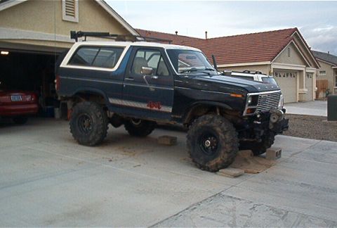 1986 Ford Bronco - This modified 1980s Ford Bronco features oversized off-road tires, a lifted suspension, and a roof rack, suggesting it's built for terrain.