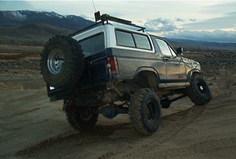 1986 Ford Bronco - 1986 Ford Bronco driving on a dirt track with mountains in the background.