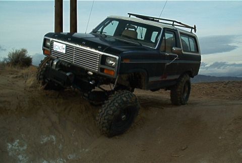 1986 Ford Bronco - This modified Ford Bronco is shown off-road, with its front end angled upwards on a sandy incline.