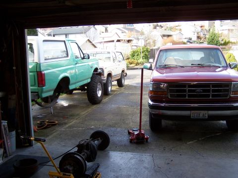 1996 Ford Bronco - Three Ford trucks are parked in a garage, with one being worked on.