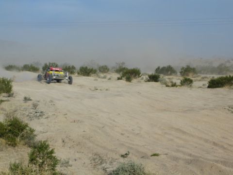 Distant red and yellow off-road buggy on a desert wash trailing dust