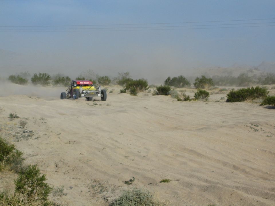 Red and yellow off-road buggy on a sandy desert rise with dust haze