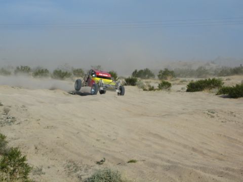 Red and yellow off-road buggy with front wheels in the air on desert sand