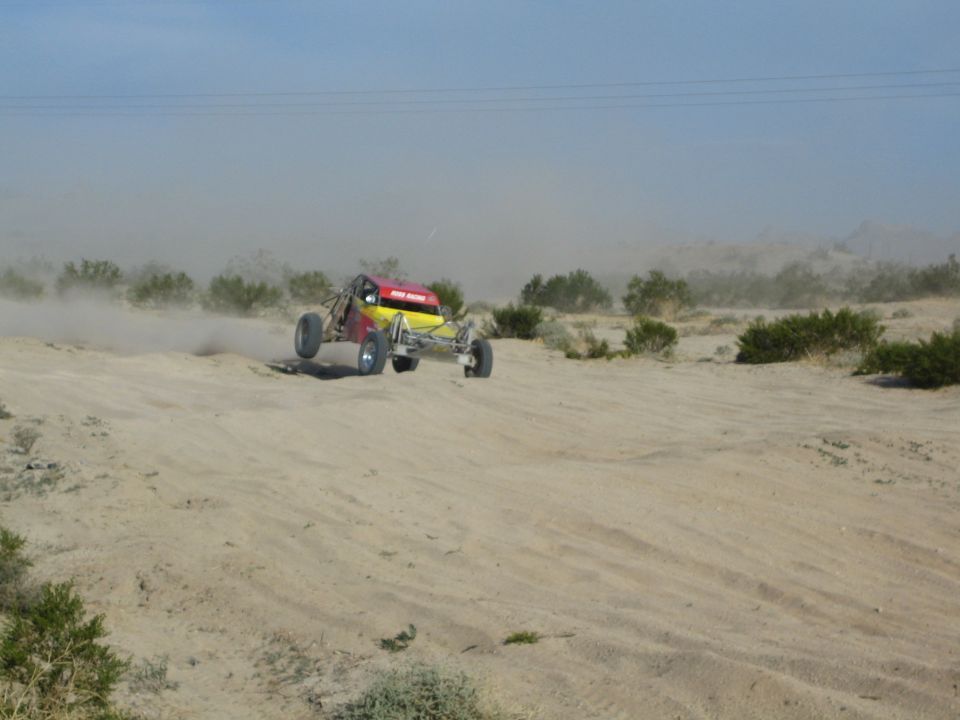 Red and yellow off-road buggy with front wheels in the air on desert sand