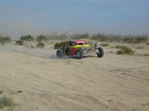 Red and yellow off-road race buggy kicking up dust on a sandy desert trail