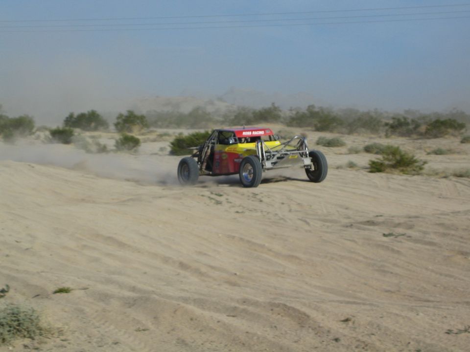 Red and yellow off-road race buggy kicking up dust on a sandy desert trail