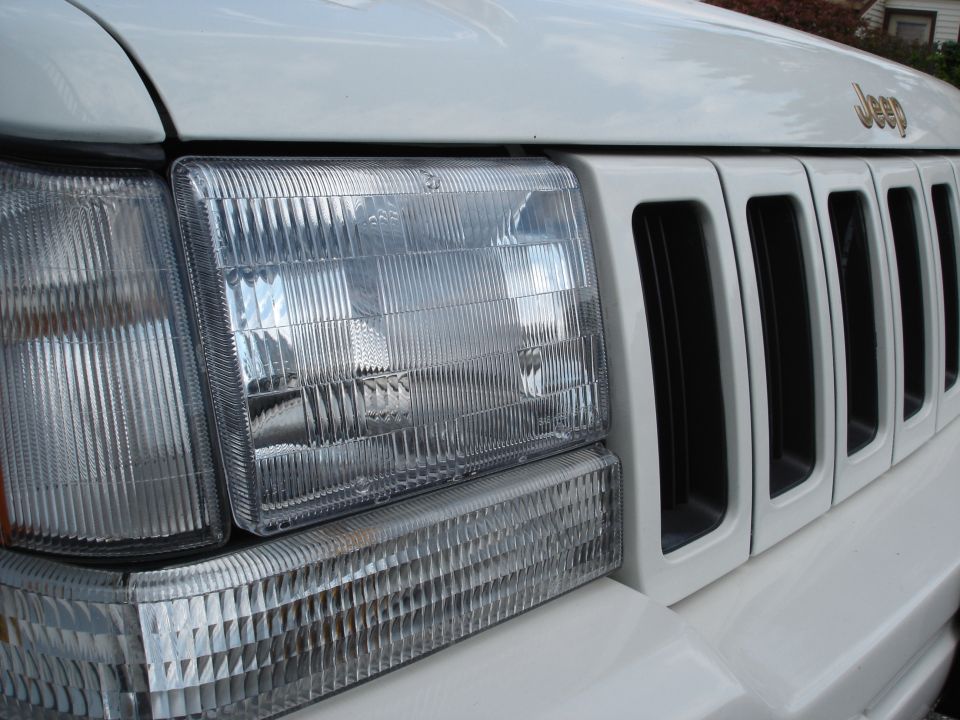 Close-up of clear headlight and seven-slot grille on a white Jeep Grand Cherokee with gold Jeep badge