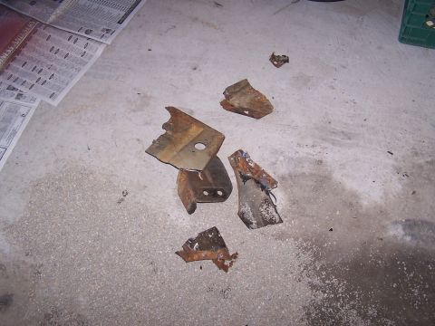 1973 Ford Ranchero - Scattered, rusted metal pieces lie on a concrete surface next to some newspapers.