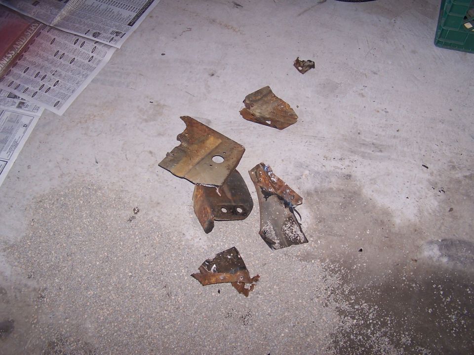 Rusty cut-out steel brackets and mounts laid out on a concrete garage floor