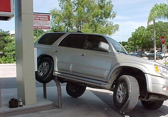 Silver SUV with front wheel on bollard at gas station