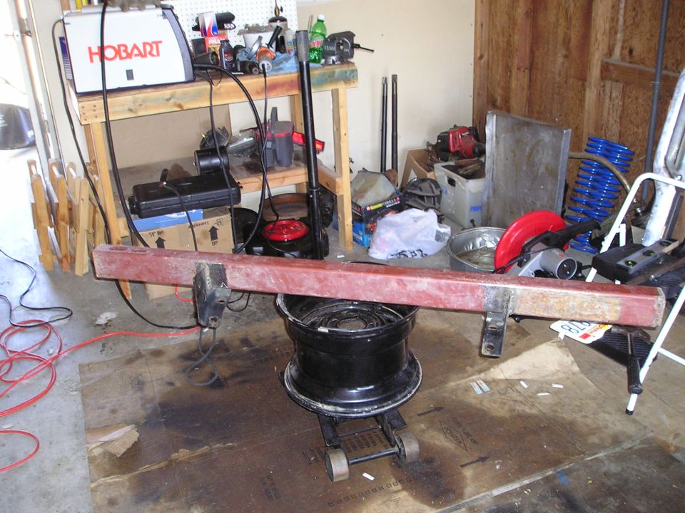 Red metal bumper on a black jack with a tire underneath, in a garage with tools and a welder