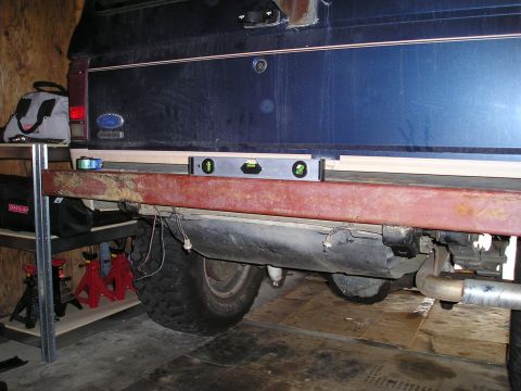 1986 Ford Bronco II - A level is used to check the alignment of the rear bumper on a vehicle, with the fuel tank visible below.