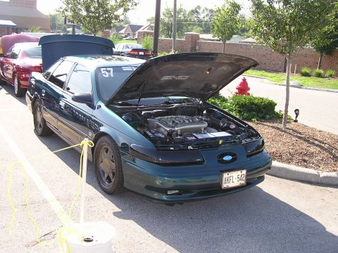 1993 Ford Taurus - A green 1993 Ford Taurus SHO is parked with its hood open, revealing the engine, as part of a car show.