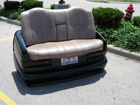 1993 Ford Taurus - A couch made from car parts, a rear bumper and license plate reading 'PLUS 91'.
