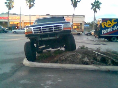 1992 Ford Bronco - This 1992 Ford Bronco is parked with its front tires on a curb and landscaping. A Rent-A-Truck is visible in the background.