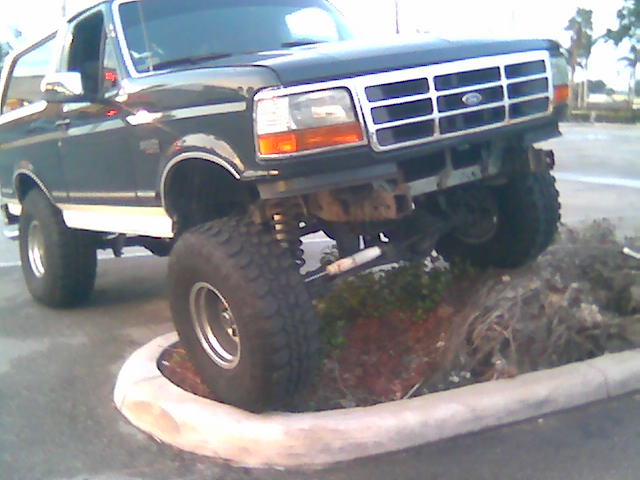 1992 Ford Bronco with lifted suspension driving over a curb