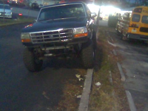 1992 Ford Bronco - This lifted Ford Bronco is parked on the side of the road next to a curb, with a school bus visible in the distance.