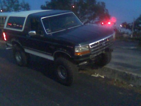 1992 Ford Bronco - A black 1992 Ford Bronco with a white top is parked on the side of the road at dusk.