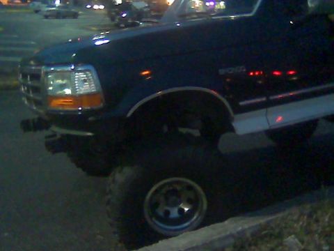 1992 Ford Bronco - A dark 1992 Ford Bronco is seen from a 3q front angle, a lifted suspension and a white stripe along its side.