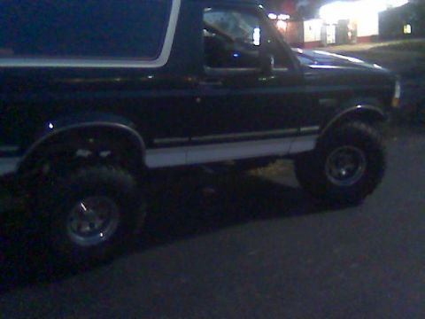 1992 Ford Bronco - A dark blue 1992 Ford Bronco with white trim and large tires is parked on a street at night.