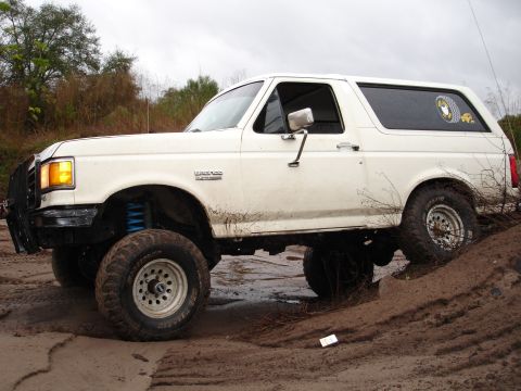 1989 Ford Bronco - This lifted 1989 Ford Bronco navigates a muddy terrain with its tires kicking up dirt.