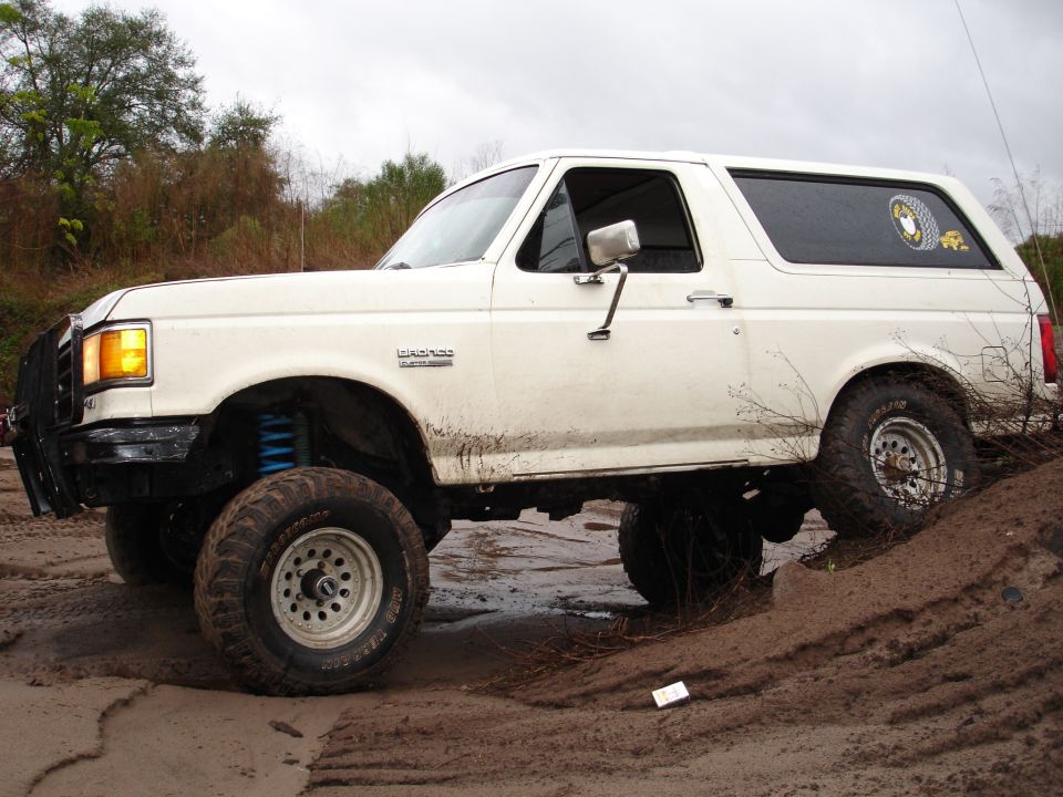 White 1989 Ford Bronco lifted and driving through mud