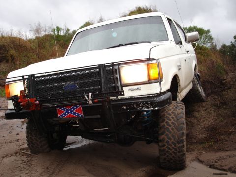 1989 Ford Bronco - White 1989 Ford Bronco navigating rough terrain with its front wheels turned.