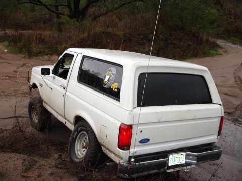 1989 Ford Bronco - This white Ford Bronco is navigating a muddy, off-road trail, with its rear end angled towards the camera.