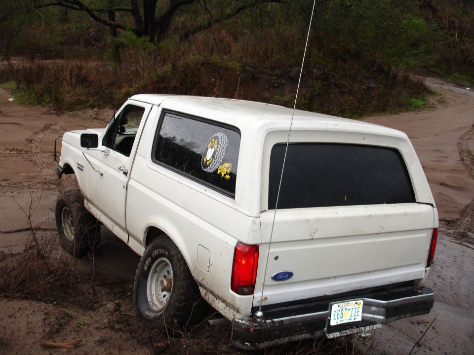 White Ford Bronco stuck in mud, rear view. License plate reads 169 TIE