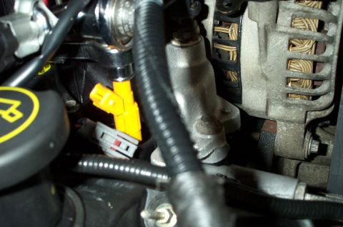 1998 Ford Crown Victoria - A close-up view of yellow fuel injectors and part of the alternator within a vehicle's engine compartment.