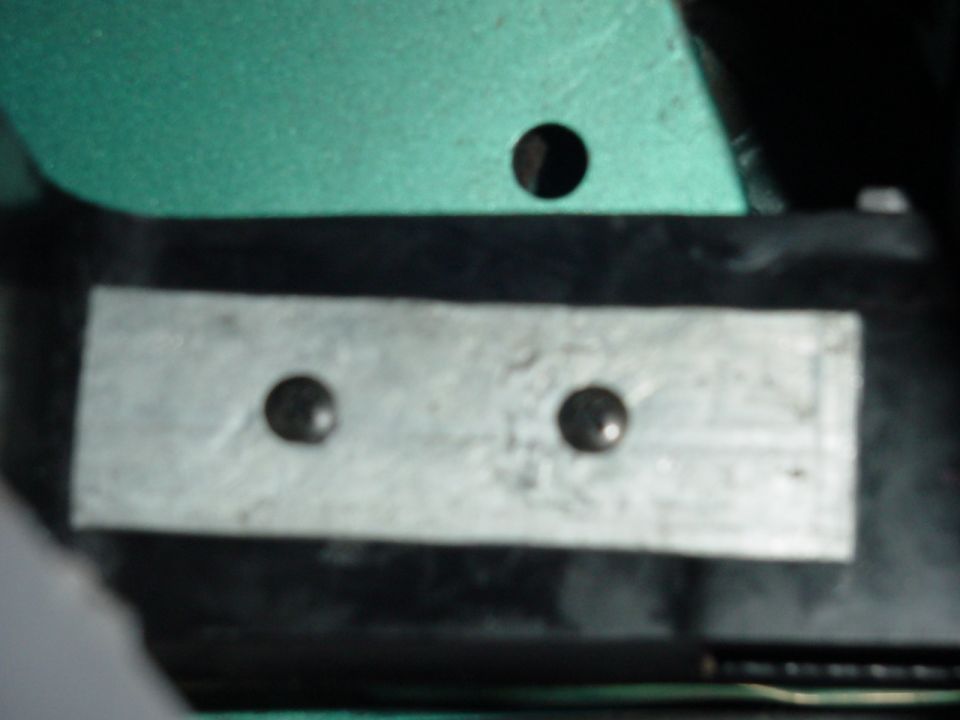 Close-up of a silver metal plate with two rivets attached to a black bracket below a green panel with a hole