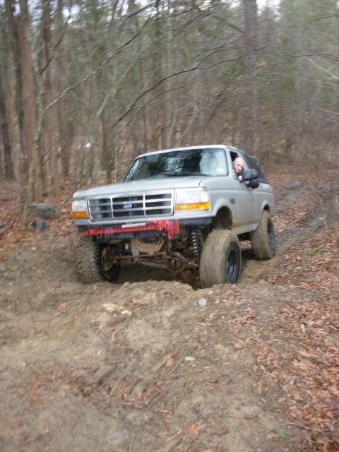 1995 Ford Bronco - A silver 1995 Ford Bronco navigates a muddy off-road trail through a wooded area.
