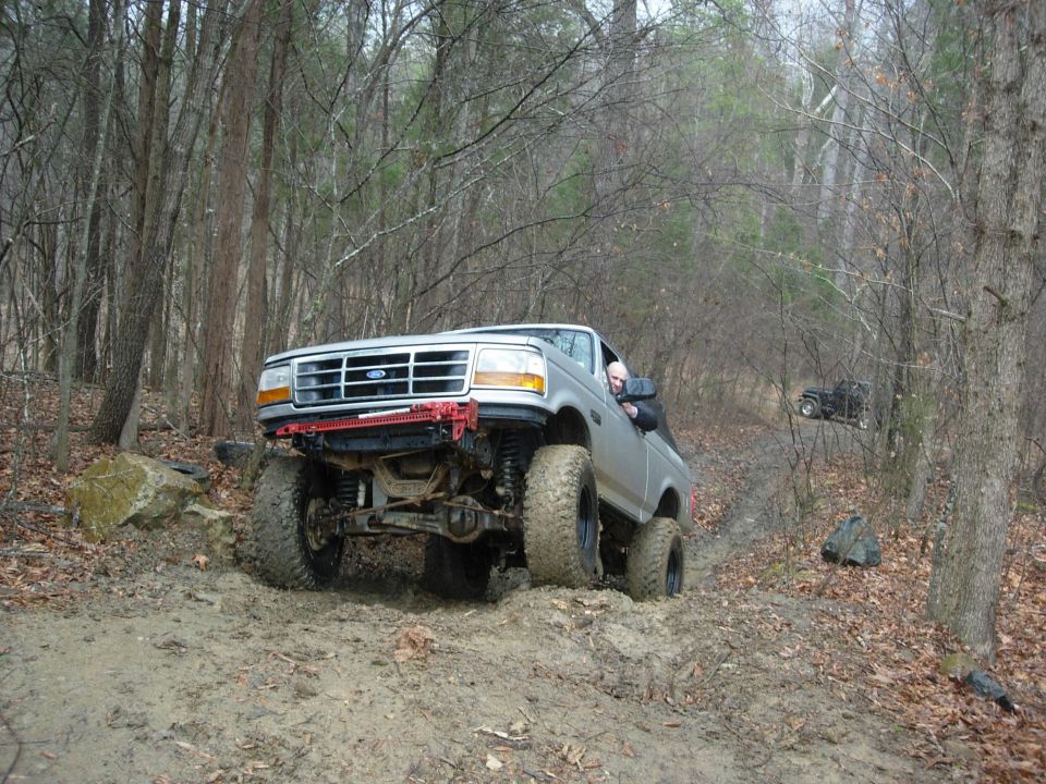 1995 Ford Bronco navigating a muddy trail with another vehicle in the background